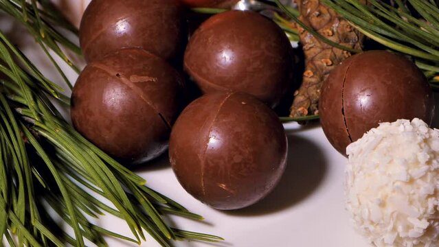 Chocolate and coconut Christmas balls - candies are spinning on the table. Pine needles for decoration. Video clips. Soft selective focus. Artificially created grain for the picture