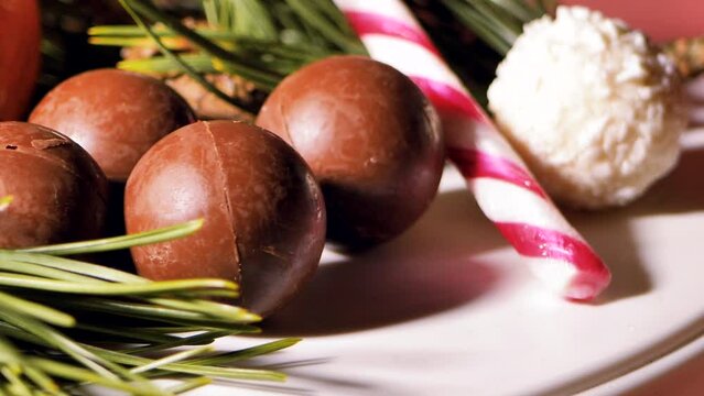 Chocolate and coconut Christmas balls - candies are spinning on the table. Pine needles for decoration. Video clips. Soft selective focus. Artificially created grain for the picture