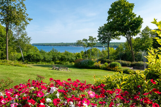Beautiful backyard scene with colorful flowers, green grass and other vegetation, a pond with a fountain, and a lake with blue water.