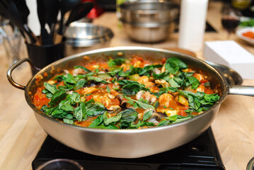 Homemade Tomato Basil Sauce in Skillet. Aromatic tomato sauce with chunks of vegetables and fresh basil leaves in a skillet on a home kitchen counter.