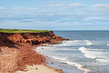 Prince Edward Island Canada north shore rugged beach coastline with waves and red rocks with cliff...