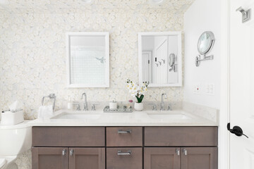 A bathroom detail with a brown cabinet, white marble countertop, and white framed mirrors on a wallpaper wall.