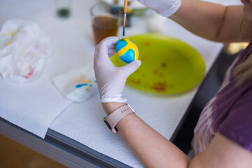 Close-up view of a woman in disposable gloves coloring a boiled egg for Easter. Sweden.