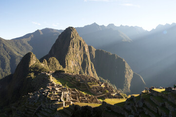 Machu Picchu mountain illuminated by the morning sun as tourists watch from the elevated part on the right of the image