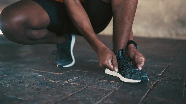 Man, hands and tie shoes for running, fitness or workout exercise on outdoor concrete floor. Closeup of African male person, runner or athlete tying shoe lace in preparation for cardio training