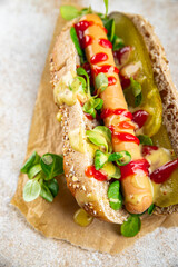 Hot Dog sausage on bun, tomato sauce, pickled cucumber, greens lettuce leaf takeaway food tasty fresh eating cooking appetizer meal food snack on the table