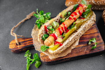 Hot Dog sausage on bun, tomato sauce, pickled cucumber, greens lettuce leaf takeaway food tasty...