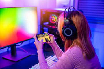 Gamer playing online game application on mobile phone wear gaming headphones, Asian woman live stream she play video game via smartphone at home neon lights living room © sorapop