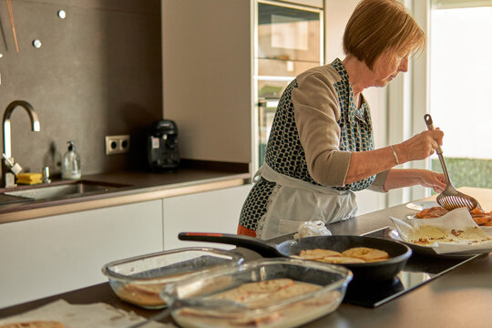 Mujer mayor cocinando torrijas para su familia durante las fiestas de Semana Santa en una cocina moderna llena de electrodom&eacute;sticos 