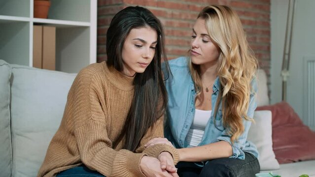 Video of pretty young woman supporting and comforting her sad friend while sitting on the sofa at home.