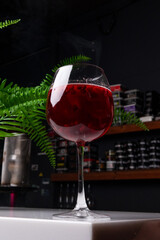 a glass with a red drink on the background of a plant in the bar