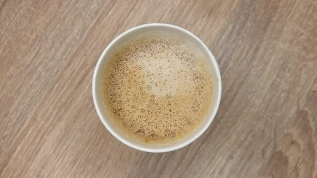 Top view of white paper disposable Irish coffee cup with foam on a wooden table in caffee house.