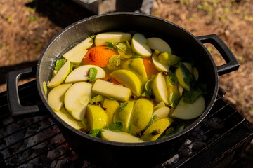 Steaming white mulled wine in a pot with sliced apples, mandarins, and fresh mint on a grill, ready for a cozy outdoor gathering