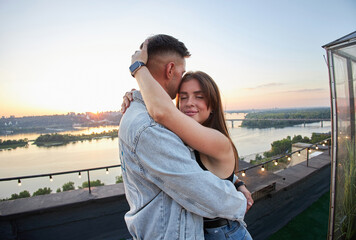 A couple shares a tender moment on a rooftop, their silhouettes etched against the evening sky.