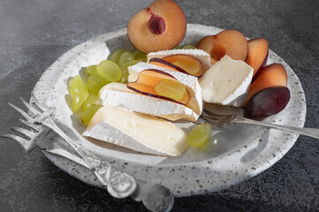 Brie camembert cheese with grapes and plums. Camembert and brie cut in chunks. The cheese is served on handmade plates