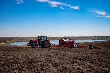 Obraz premium Red tractor with red planter sowing corn in a field