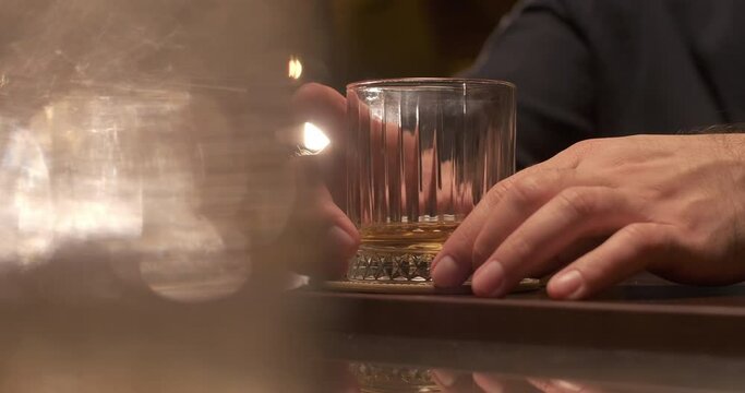 Adult man with a glass of whiskey or brandy at the bar in the evening. Enjoy fine alcoholic drinks beverage. Slow motion