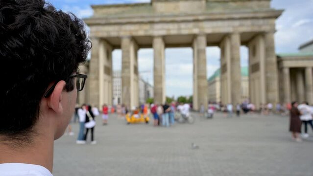Berlin, Germany, August 10, 2023. Footage at the Brandenburg Gate: a young tourist looks around and then takes a photo with his cell phone. Travel destinations, lifestyles.