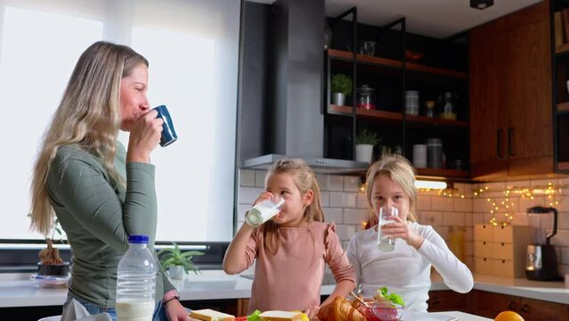 Charming kitchen scene: two adorable girls and their beautiful mom share smiles while enjoying a morning glass of milk. A delightful family moment captured.