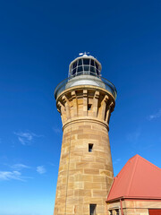 Lighthouse and red roof on the island at daytime. Sandstone lighthouse at the top of a hill. Coast ligthouse against a blue sky. Lighthouse in the harbor. Lighthouse on the coast of the region sea.