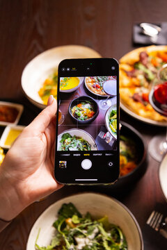 a hand with a phone takes pictures of food at the table