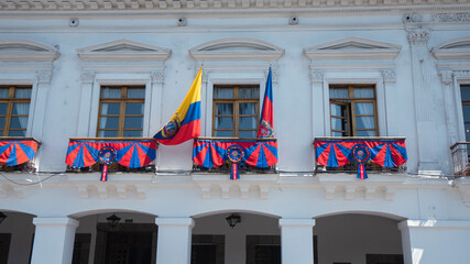 Close-up of white house balconies decorated with flags of Quito and the flag of Ecuador