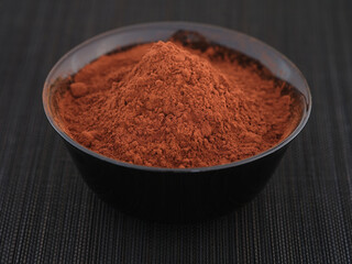 Organic cocoa powder in a black bowl. Close up.