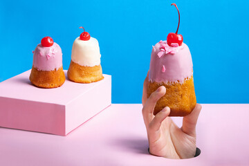 A woman's hand steals a cake through a hole on a pink and blue background