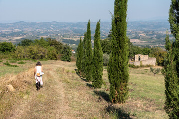 Fototapeta na wymiar Awoman walking with her dog on a rural path beetween Tuscan fields