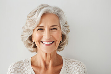 Portrait of beautiful older woman smiling and standing by white wall. A place for text, a banner for advertising.