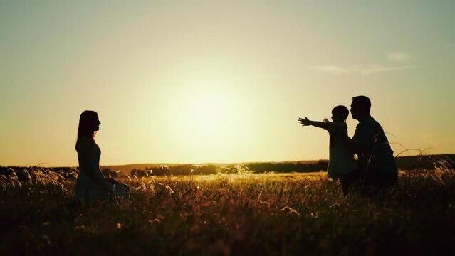 Parents with child playing after delightful picnic on nature in field at sunset. Parents hugging daughter on summer holiday. Parents with daughter go to vacation to spend time in family circle
