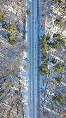 Railway tracks through the forest in snow, empty railway traction, concept of train delays due to winter weather conditions, vertical, aerial view.