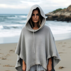 A woman wearing poncho with hoodie on the beach.