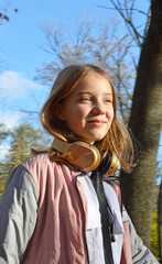 Fototapeta premium a girl walks in the fresh air in an autumn park, headphones on her neck. there is a happy smile on the face. child listens to music or audiobook. hobbies, recreation and entertainment