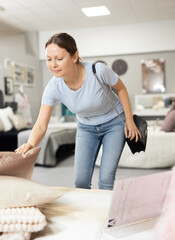 In furniture store, woman examines mattress and sleeping accessories, bedspread pillows cushion....