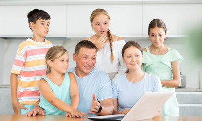 Husband, wife and children sit in front of laptop screen and communicate via video and relatives. Convenient and accessible communication with family and friends at any time of day