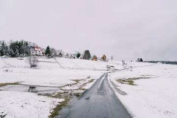 Fotobehang Asphalt road in a snowy village on a hill © Nadtochiy