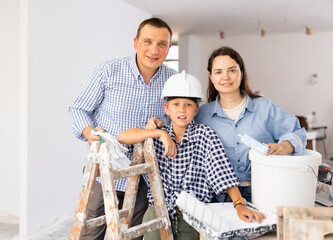 Portrait of family doing renovation at new home, holding tools for wall painting, posing together and smiling
