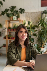 Young plant store worker posing at her workplace while working on laptop