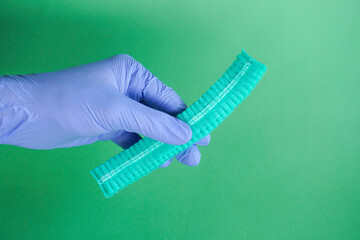 medical officer wearing blue medical gloves is holding a green surgical cap that has not been opened, isolated on green