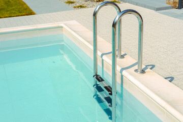 Grab bars ladder in the blue swimming pool. Ladder stainless handrails for descent into swimming...