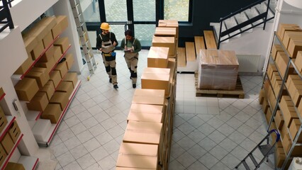 Aerial drone shot of warehouse laborers inspecting cardboard box packages , ensuring they are ready...