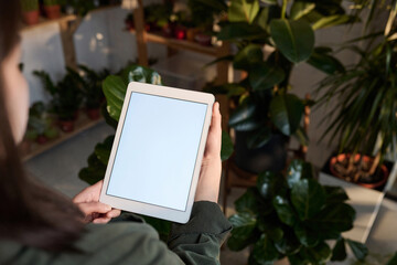 Mockup image of woman holding digital tablet with blank screen standing at plant store