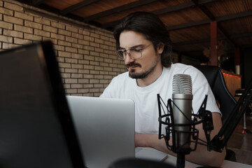 A podcaster meticulously edits audio on a laptop in a home studio setup, with a professional...