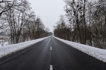 Panorama ulicy zimą, droga biegnąca wzdłuż kadru w śnieżny dzień o wieczornej porze w...