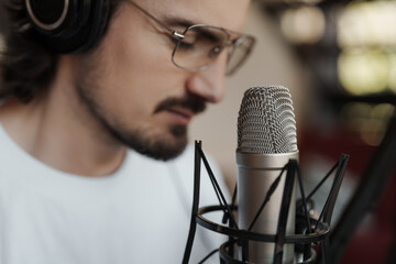 Close-up of a male artist with headphones performing or recording vocals with a studio microphone