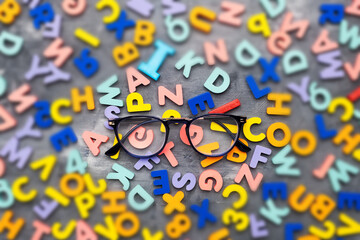 Reading glasses on a gray background surrounded by multi-colored letters and numbers. The concept of restoring vision and health.