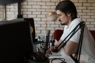 Intense focus as a sound engineer adjusts settings on a laptop in a studio with professional...