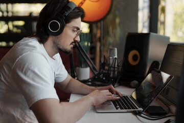 A music producer is deeply focused on mixing tracks on his laptop in a cozy studio with ambient...