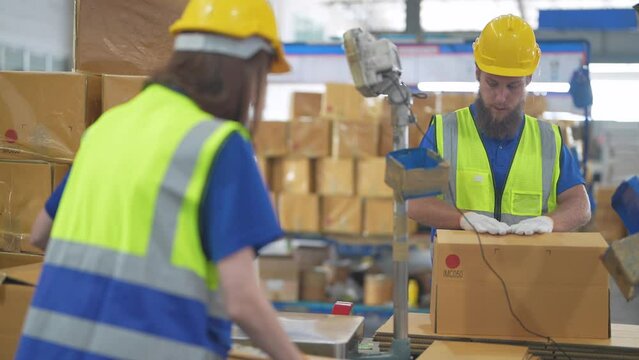 Warehouse Worker Folding Paper Box For Packing The Items In A Large Warehouse. Man Sealing Cardboard Boxes For Shipping In Cargo Product Stock.